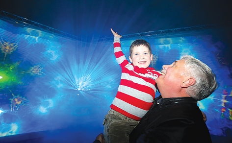 Kelvin Sparks helps his grandson Luke Foord, 7, reach up to the light beams coming off a display at Light Nelson on Sunday. Photo: Phillip Rollo.